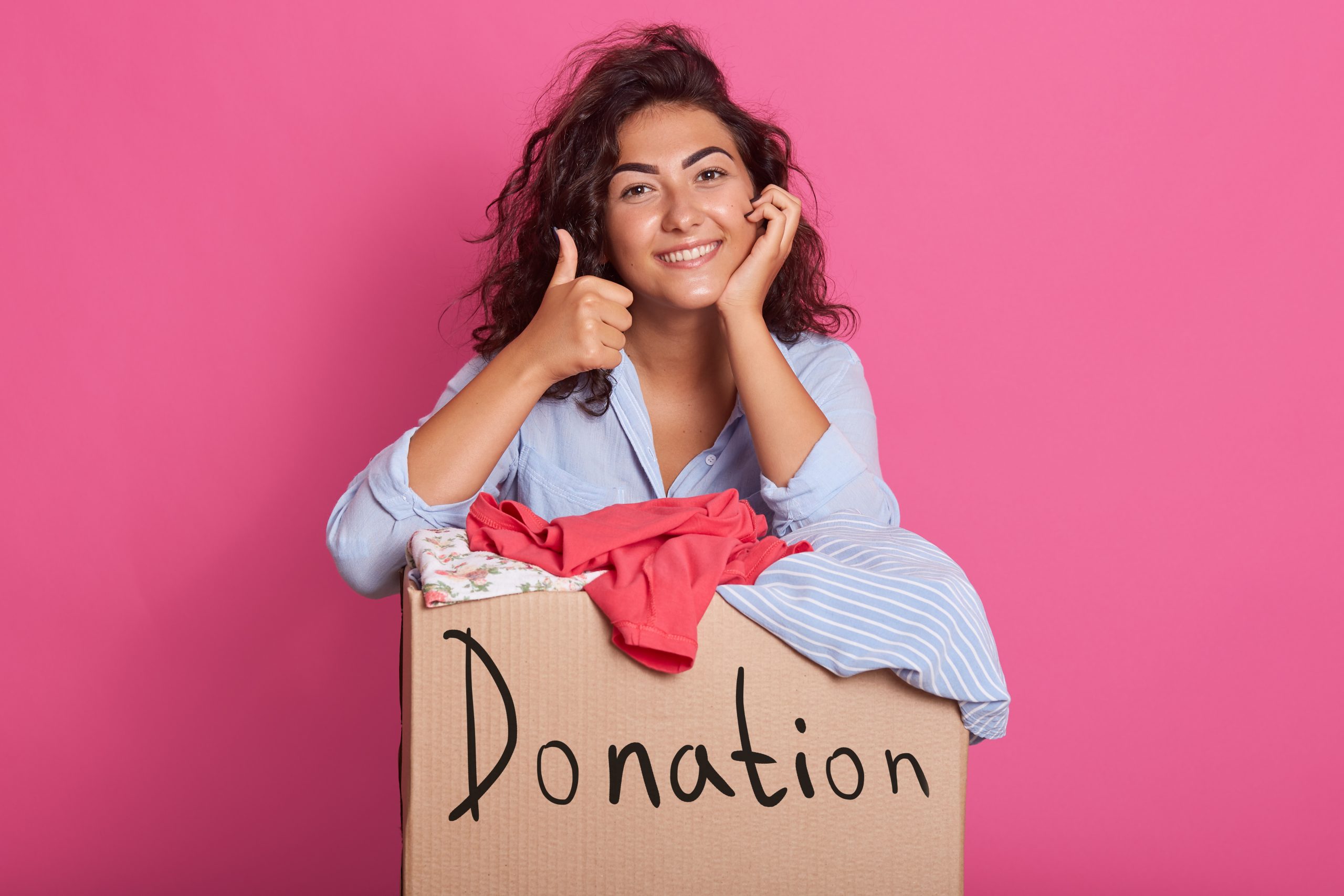 Portrait of happy young woman with clothes donation standing over rosy